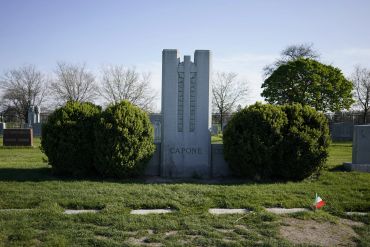 Gravestone of Al Capone in a cemetery surrounded by bushes.