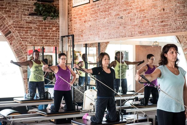 Reformer class doing intermediate kneeling arm exercise.