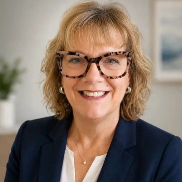 Smiling woman with glasses wearing a blazer in a professional setting.