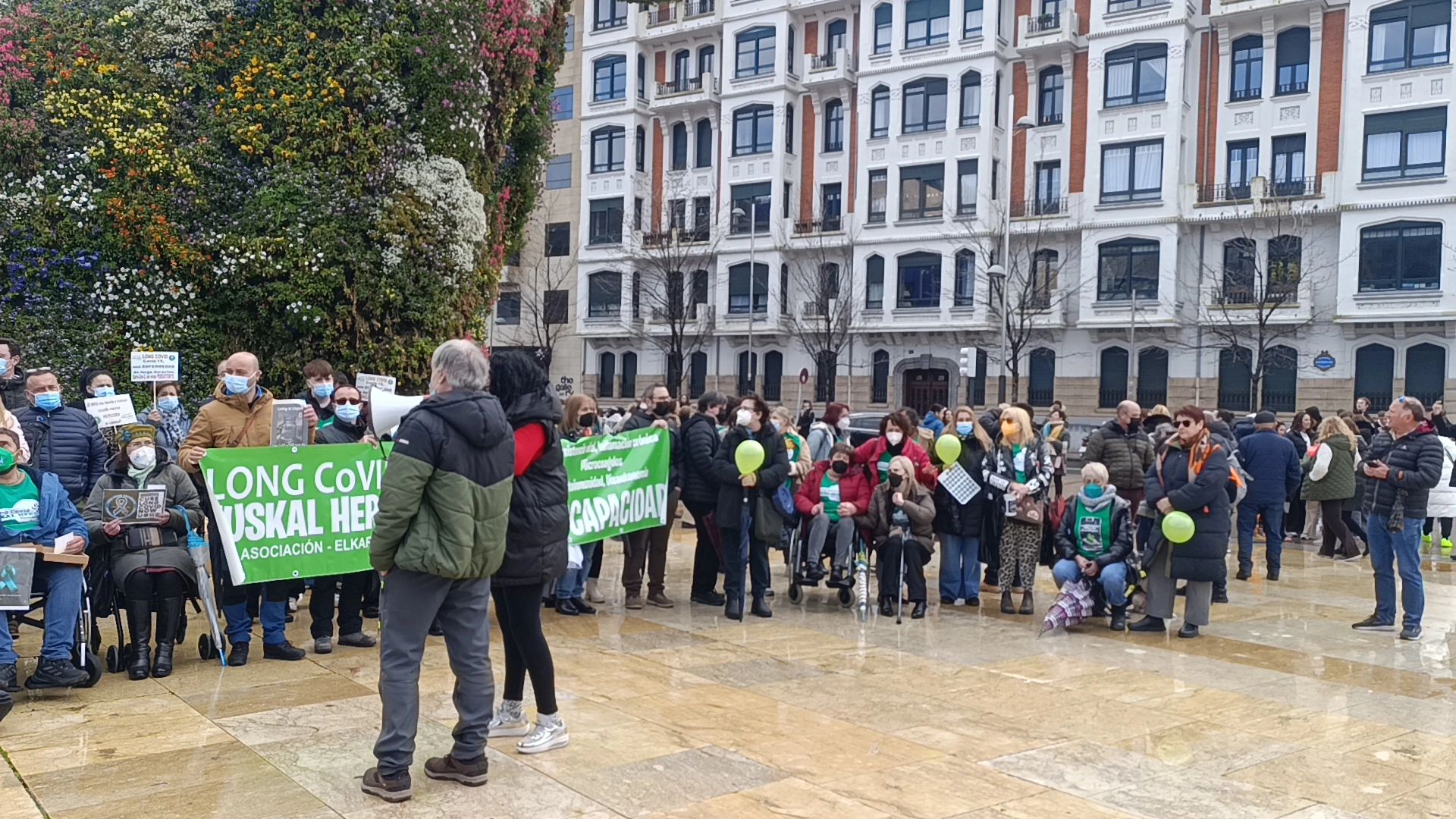 A group of people protesting for Long COVID support in a city square.