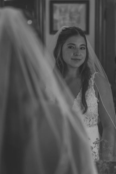Bride gazing at her reflection in a mirror, wearing a lace wedding dress and veil.