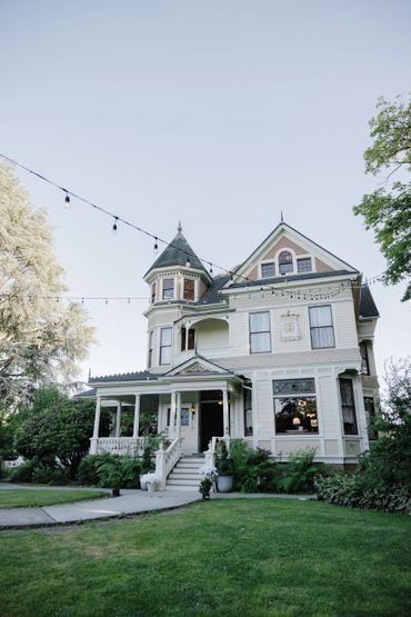 Elegant Victorian-style house with turret and porch, decorated with hanging string lights.