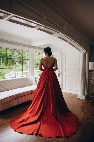 Woman in an elegant red gown standing by a window in a stylish room.