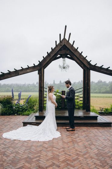 Couple exchanging vows under rustic wooden archway outdoors.