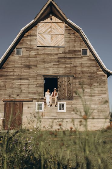 Couple sitting on a wooden barn window ledge on a sunny day.