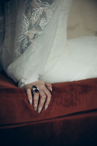 Elegant hand with a sapphire ring and lace sleeve on a red velvet surface.