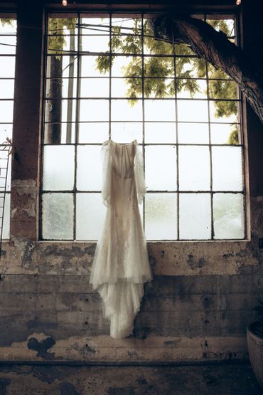 Elegant wedding dress hanging in front of a large rustic window.