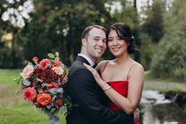 Couple embracing outdoors with a vibrant bouquet and serene nature background.
