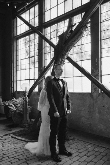 Black and white photo of a bride and groom standing back to back in an industrial setting.