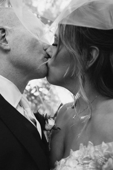 Black and white photo of a bride and groom sharing a kiss under a veil.