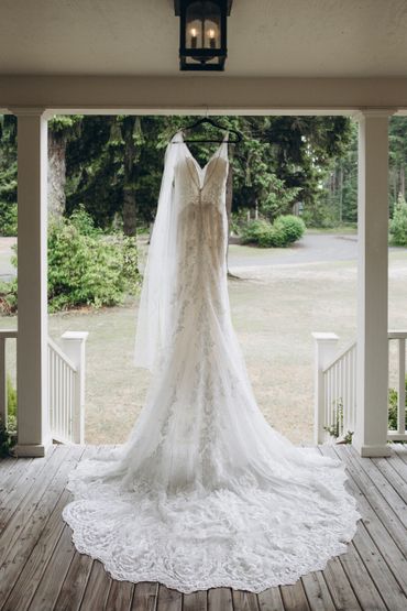 Elegant lace wedding dress hanging on porch with nature backdrop.