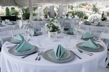 Elegantly set round table with mint green napkins and white floral centerpiece.