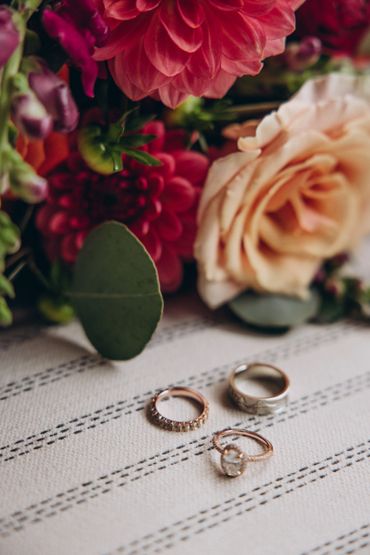 Three elegant rings placed on a textured cloth with vibrant flowers in the background.