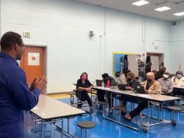 A person presenting to an attentive group in a school cafeteria.