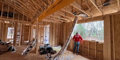 A man in a red jacket stands inside a wooden house under construction.