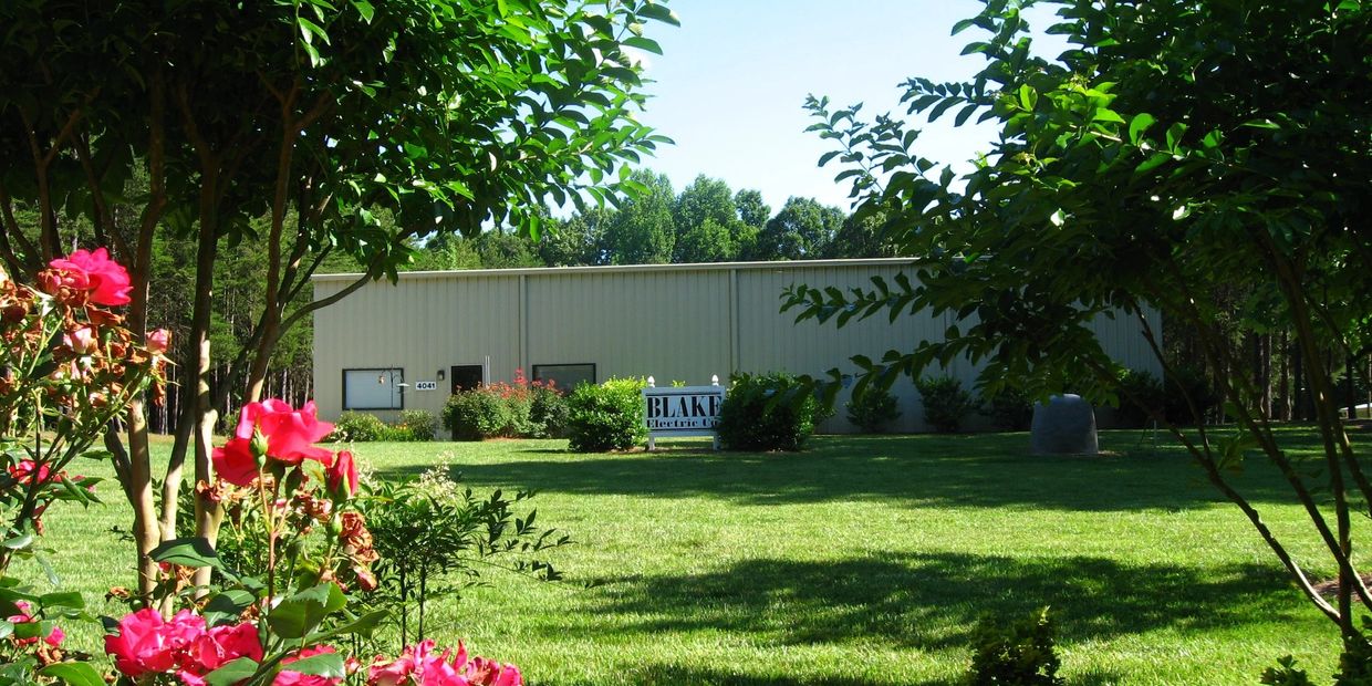 Bright pink flowers and green trees frame a beige industrial building under clear blue sky.