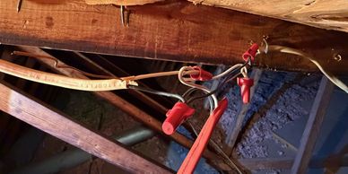 Red insulated electrical connectors and cables attached to wooden beams in an attic.