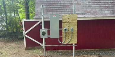 Electrical panel setup mounted on a wooden and metal frame outside a red barn.