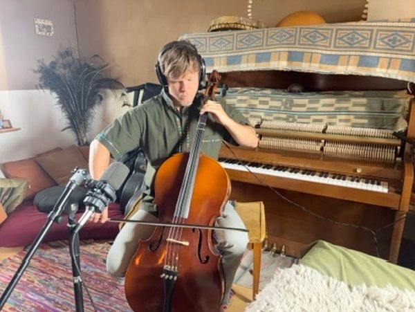 Young man playing cello with headphones on indoors.