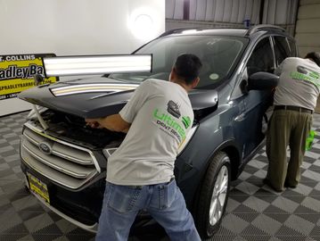 Two workers repairing a black Ford SUV in a garage.