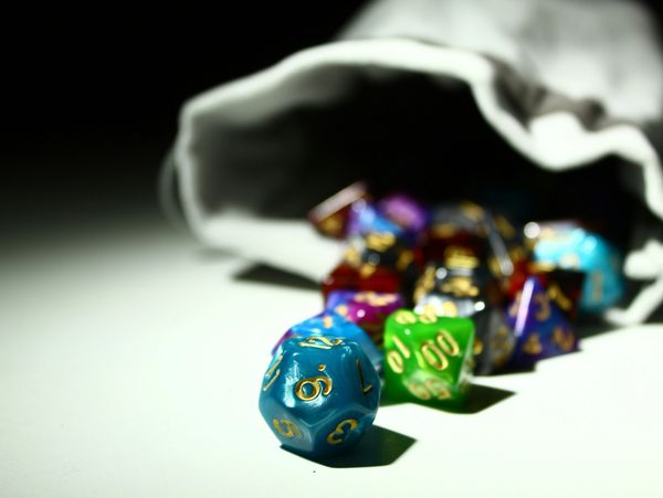 Colorful polyhedral dice spilling from a bag on a white surface.