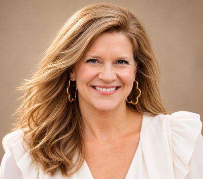 Smiling blonde woman with wavy hair and gold earrings.