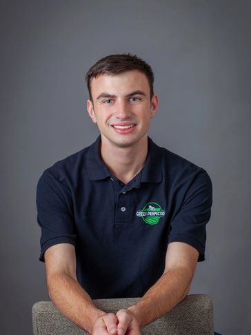 Young man in a navy polo shirt smiling, seated against a gray background.