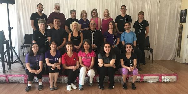 Group photo of people posing indoors, smiling and seated in three rows.
