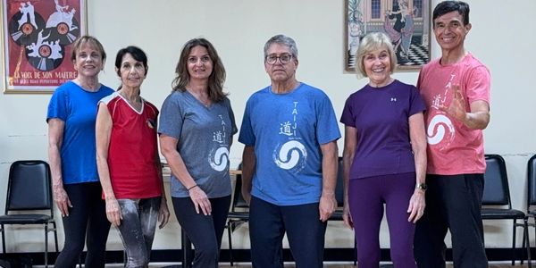 Group of six adults posing in casual athletic wear indoors.