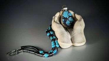 A turquoise pendant held by a white hand-shaped stand with matching beaded necklace.