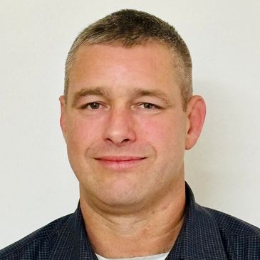 Portrait of a smiling man with short hair against a plain background.