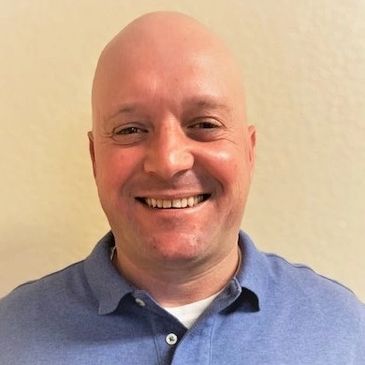 Smiling bald man in a blue polo shirt against a plain background.