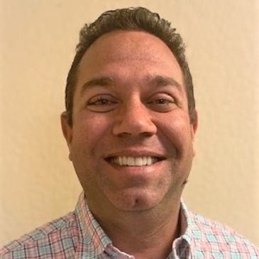 Smiling man with short hair wearing a checkered shirt.