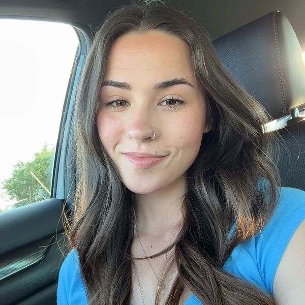 Young woman with long brown hair and nose ring smiling inside a car.