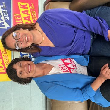 Two smiling women sitting together in front of colorful campaign signs.