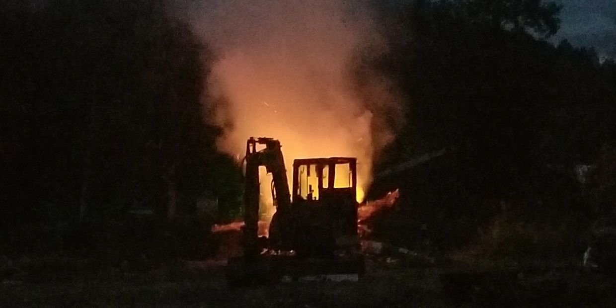 Excavator on jobsite with burning brush pile behind
