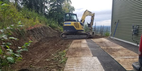 Excavator digging and grading to extend parking area into hill