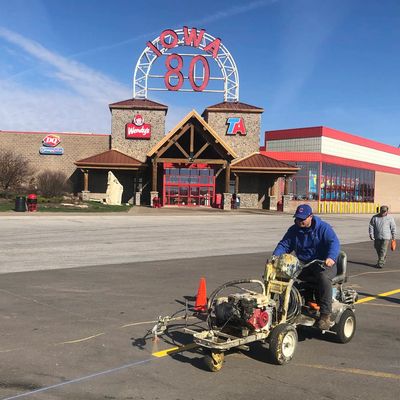A man operates a line painting machine in front of a travel plaza with Wendy's and Dairy Queen signs.