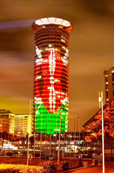 Kenyan flag displayed on a tall building illuminated at night.