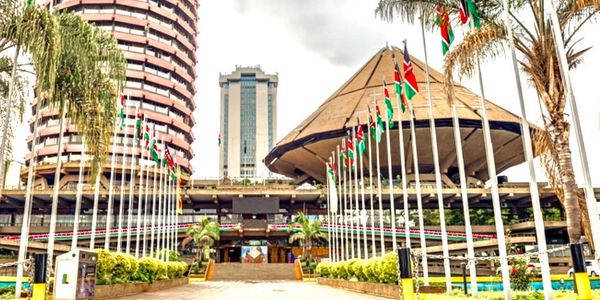 Kenyan Parliament buildings adorned with national flags under a cloudy sky.