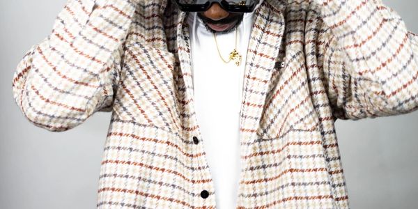 Person wearing a plaid jacket and sunglasses, adjusting the jacket collar.