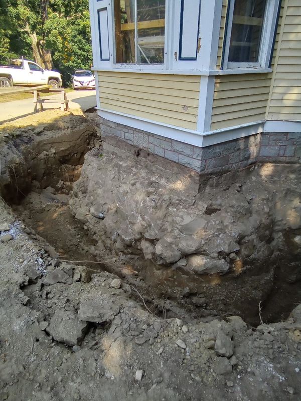 Excavation around a house foundation exposing stone and dirt.