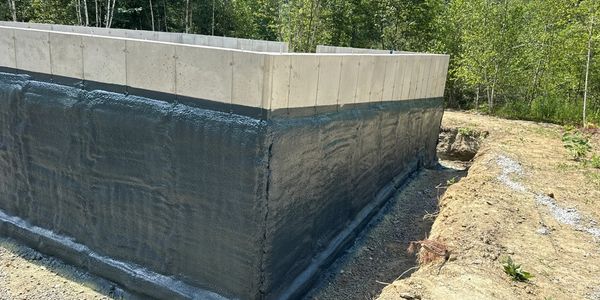 Concrete foundation wall coated with waterproofing material in a forested area.