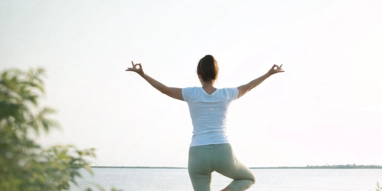 Woman practicing yoga by a calm lake at sunrise or sunset.
