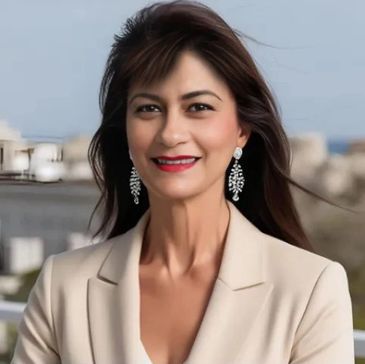 Confident woman with earrings smiles outdoors in a beige blazer.