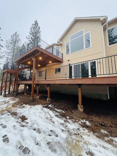 A beige house with a wooden deck and snow-covered ground.