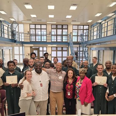 Group photo of diverse individuals in a large, bright institutional room holding certificates.