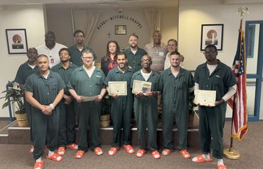 Group photo of men in green uniforms holding certificates, standing in a chapel.