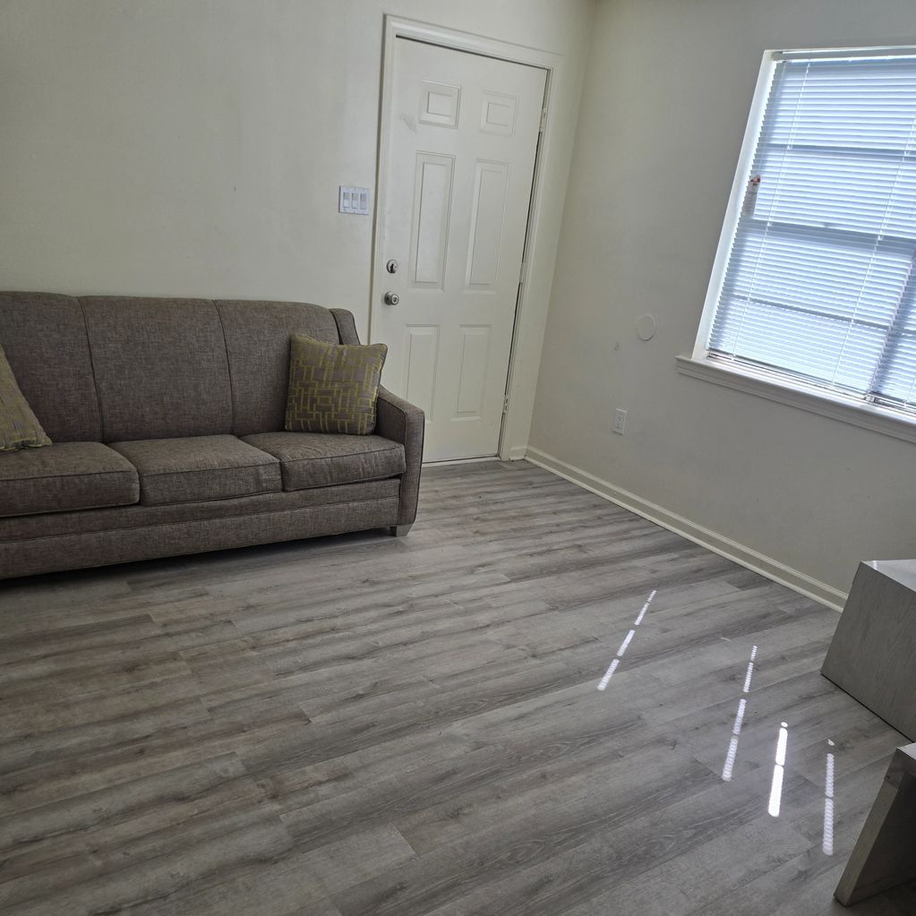 Minimalist living room with gray couch and wood flooring.