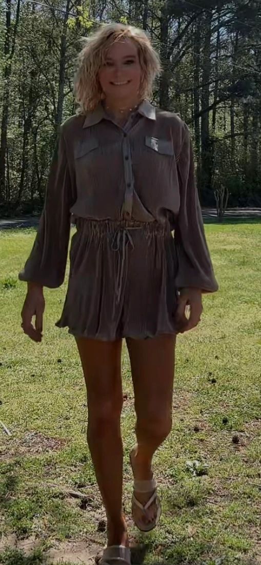 Smiling woman walking outdoors in a casual, loose-fitting outfit with shorts and sandals.